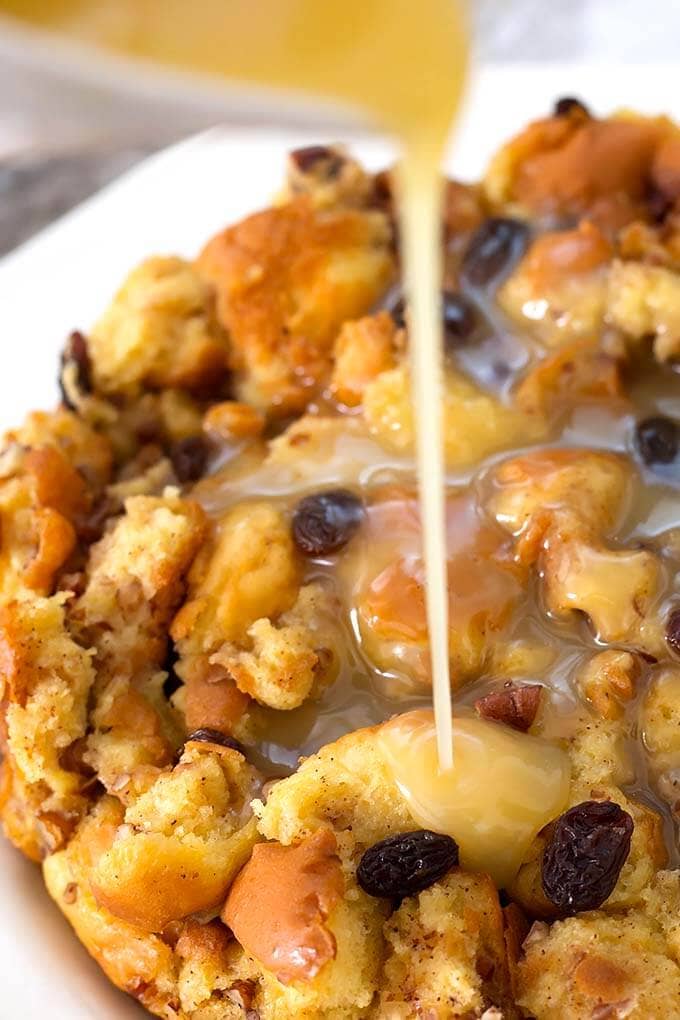 Bread Pudding on a white plate with custard pouring on top