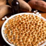 Instant Pot Candied Yams in white bowl on wood board next to marshmallows and yams