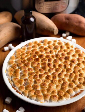 Instant Pot Candied Yams in white bowl on wood board next to marshmallows and yams