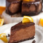 Slice of Instant Pot Chocolate Orange Cheesecake on a white plate garnished with orange slices and chocolate chips