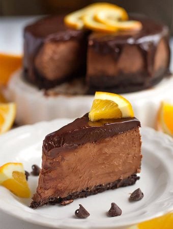 Slice of Instant Pot Chocolate Orange Cheesecake on a white plate garnished with orange slices and chocolate chips