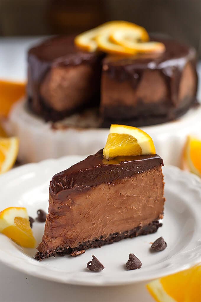 Slice of Instant Pot Chocolate Orange Cheesecake on a white plate garnished with orange slices and chocolate chips