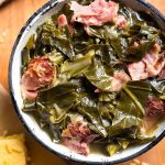 Instant Pot Collard Greens with a ham hock in a bowl with black rim on wooden board