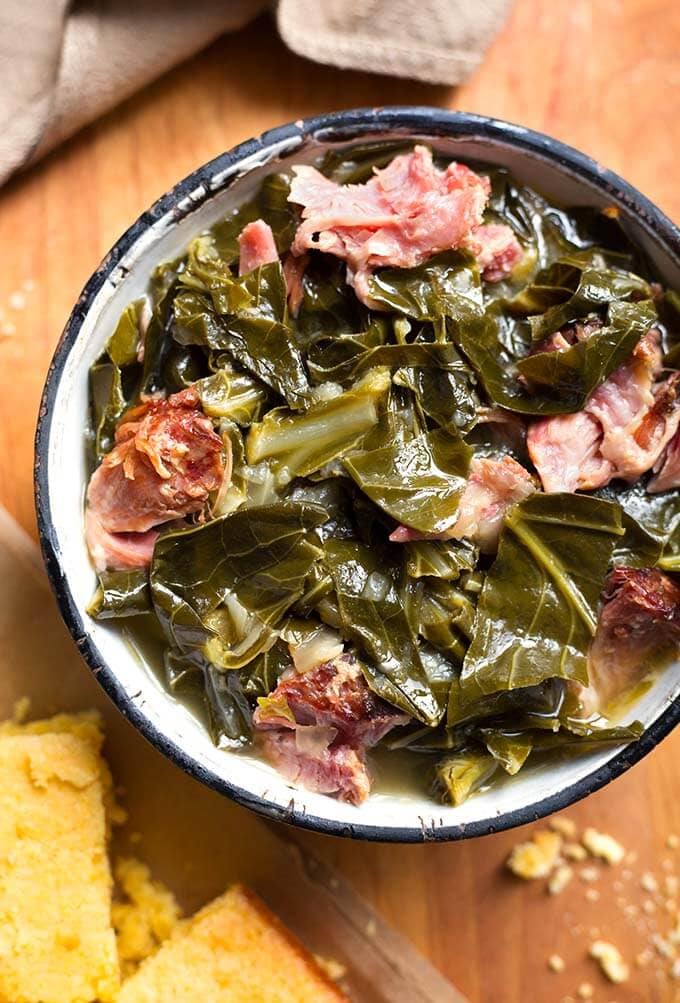 Instant Pot Collard Greens with a ham hock in a bowl with black rim on wooden board