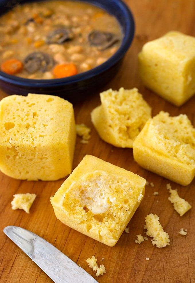 Cornbread Squares next to a knife and blue bowl of soup on a wooden board