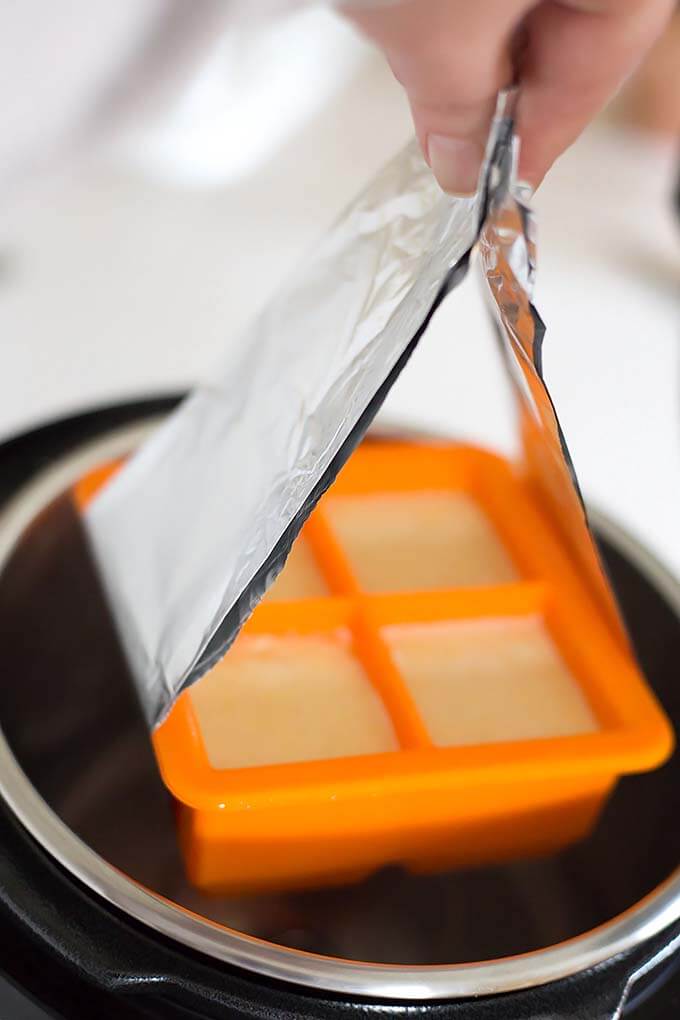 Cornbread Squares in orange baking mold being lifted from pressure cooker with aluminum sling