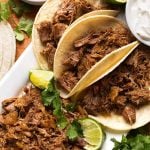 Pork Carnitas in small tortillas on a white platter garnished with lime and cilantro