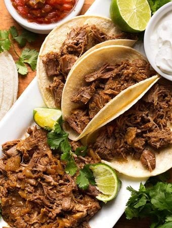 Pork Carnitas in small tortillas on a white platter garnished with lime and cilantro