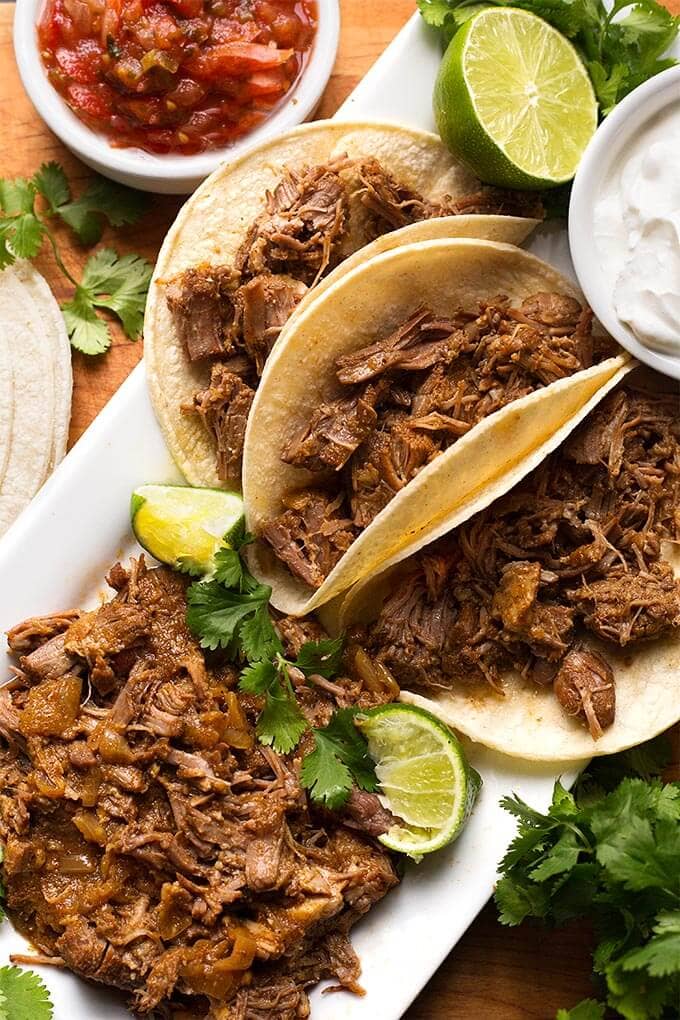 Pork Carnitas on a white rectangular platter with three corn tortillas filled with meat filling