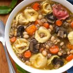 Tortellini Soup in a white bowl on wooden board with spoon