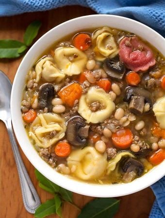 Tortellini Soup in a white bowl on wooden board with spoon