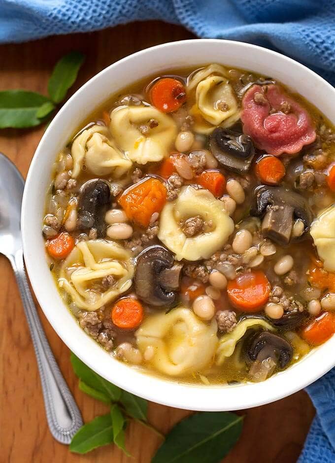 Tortellini Soup in a white bowl on wooden board with spoon