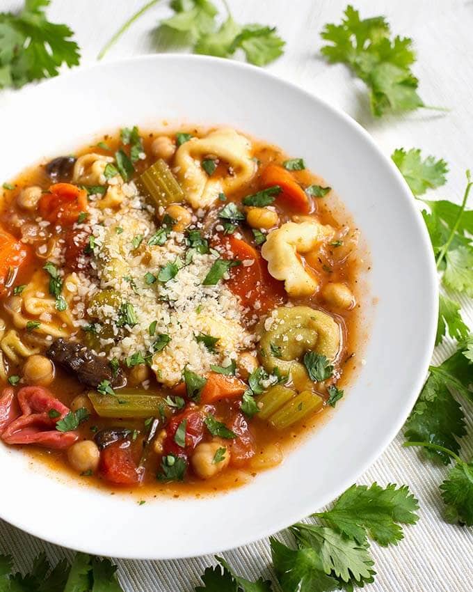 vegetable tortellini soup in a white bowl surrounded by parsley