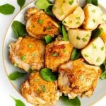 Instant Pot Chicken Thighs and potatoes on a white plate with brown rim sprinkled with baby spinach