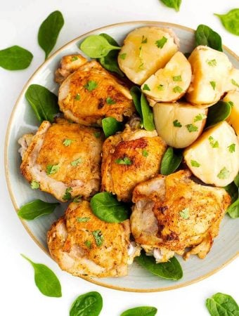 Instant Pot Chicken Thighs and potatoes on a white plate with brown rim sprinkled with baby spinach