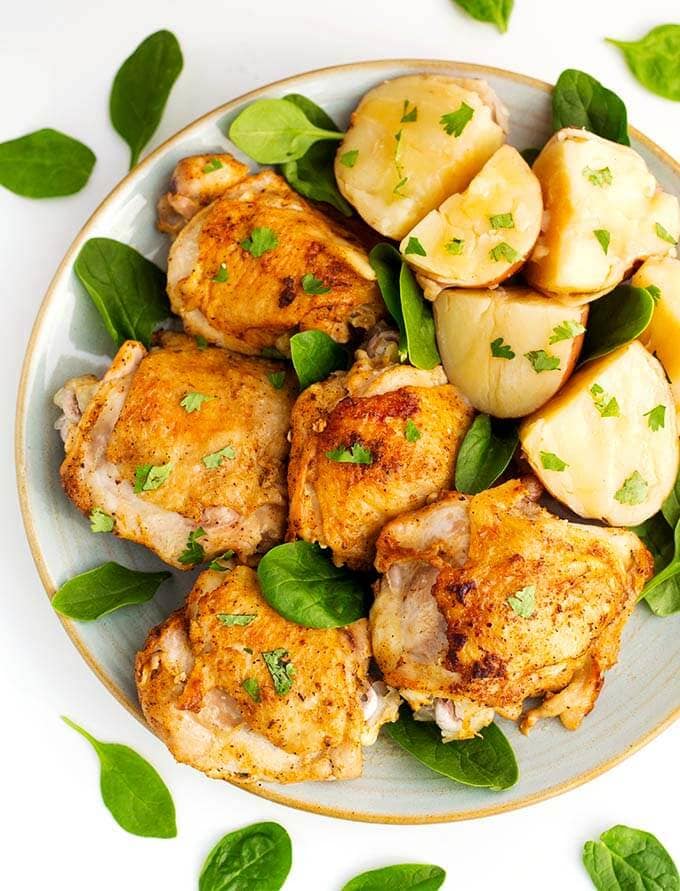 Instant Pot Chicken Thighs and potatoes on a white plate with brown rim sprinkled with baby leafed spinach 