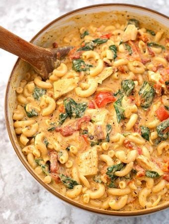 Creamy Garlic Tuscan Chicken Pasta in beige bowl with wooden spoon