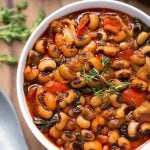 Black-Eyed Peas in a white bowl next to spoon on wooden board