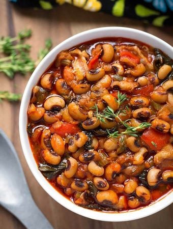 Black-Eyed Peas in a white bowl next to spoon on wooden board