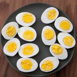 Boiled Eggs cut in half on black plate on wood board