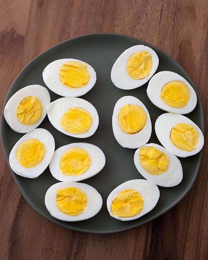 Boiled Eggs cut in half on black plate on wood board