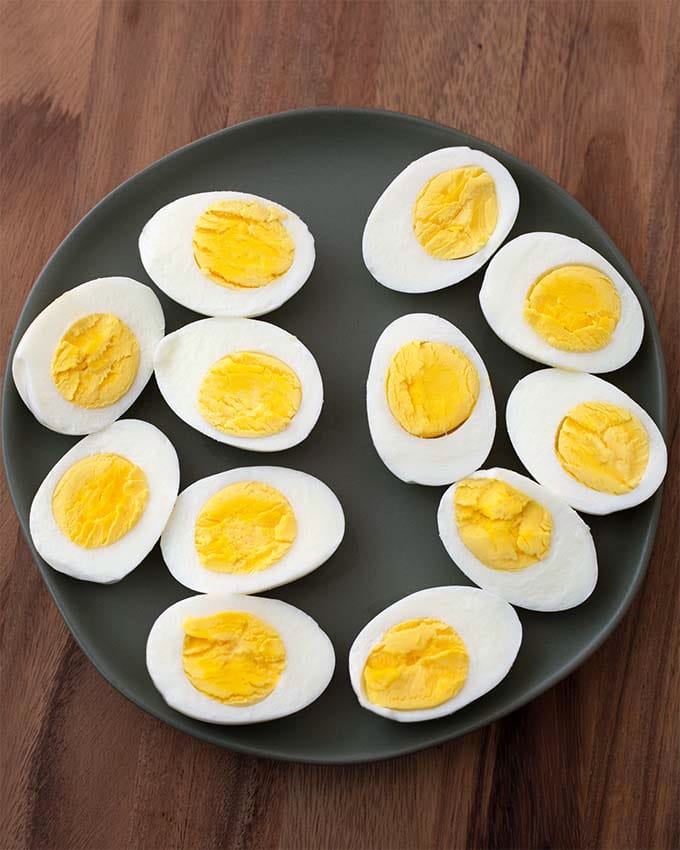Instant Pot Boiled Eggs cut in half on black plate on wood board