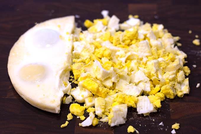 Egg loaf cut in half with one side crumbled to pieces on dark wood background