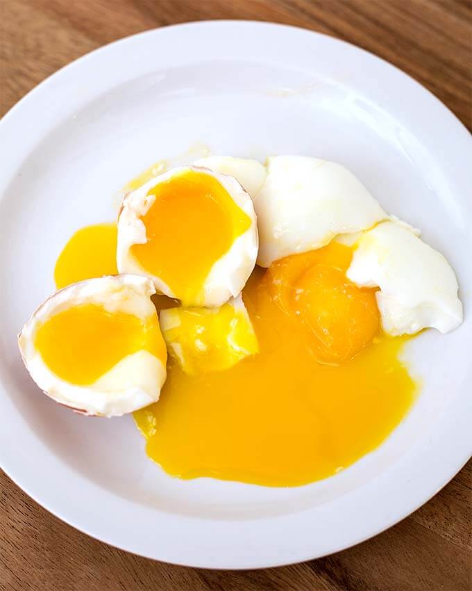 Two soft Boiled Eggs cut in half on white plate on wooden board