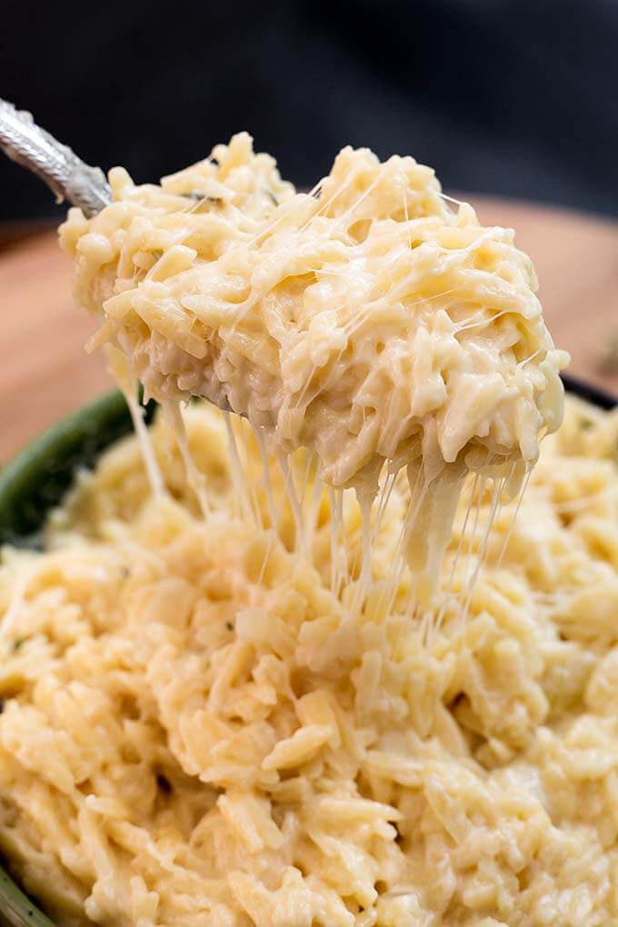 Close up of a spoonful of Cheesy Garlic Orzo pasta over green bowl