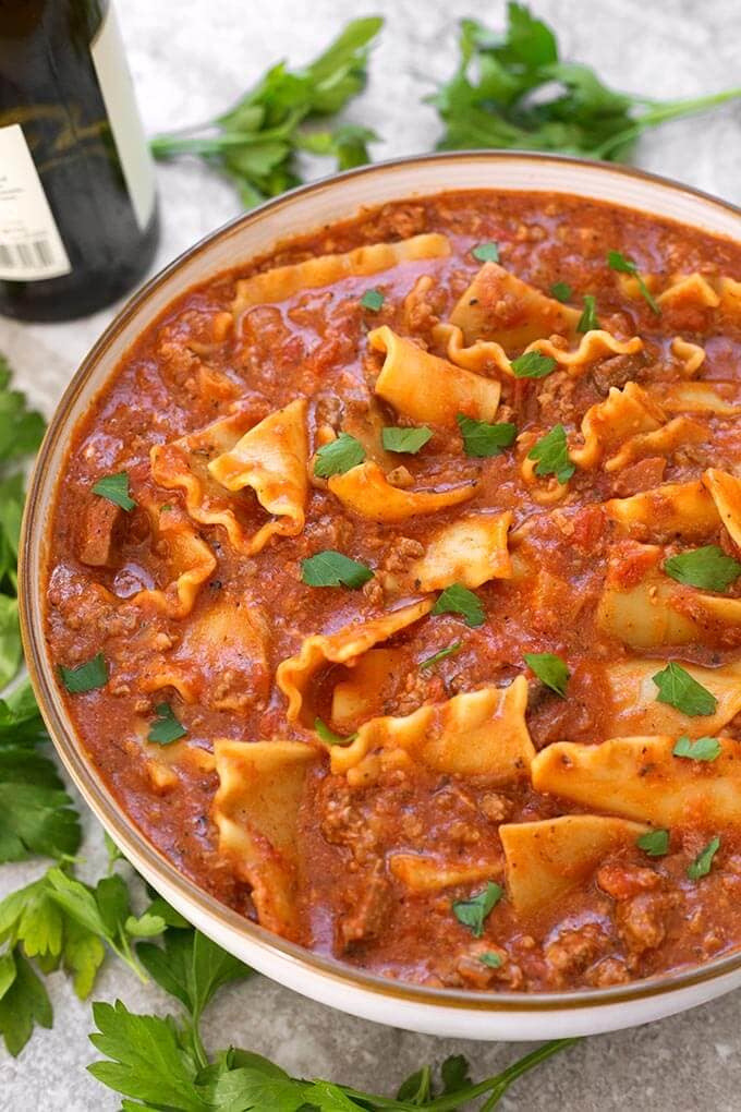 Easy Lasagna Soup in a white bowl with brown rim surrounded by parsley