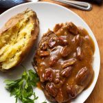 Maple Mustard Pork Chops with baked potato and parsley on a white plate on wooden board next to fork and knife