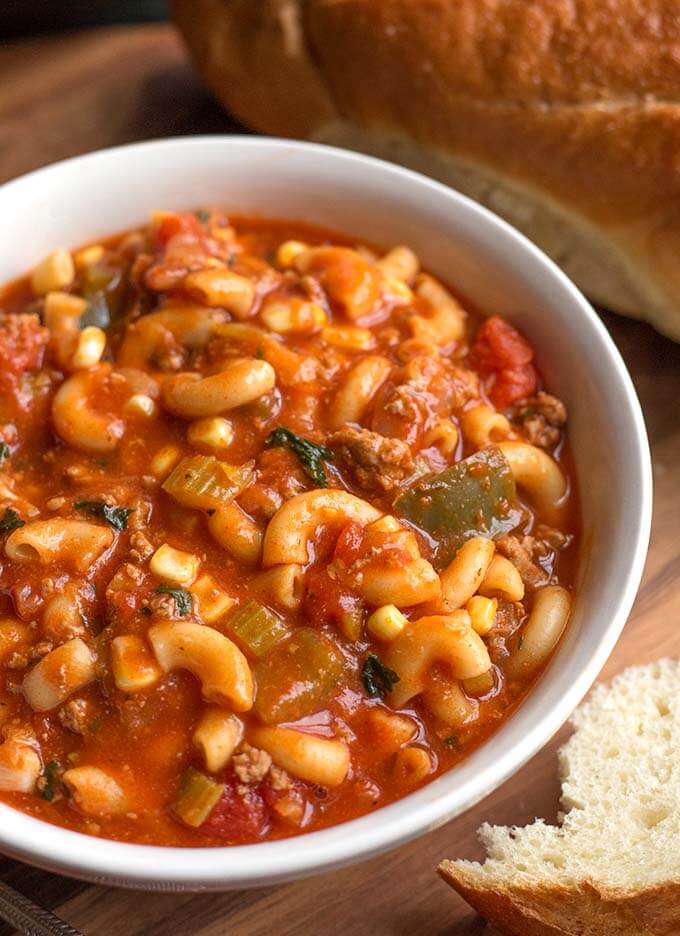 American Goulash in a white bowl on wooden board with bread chunk