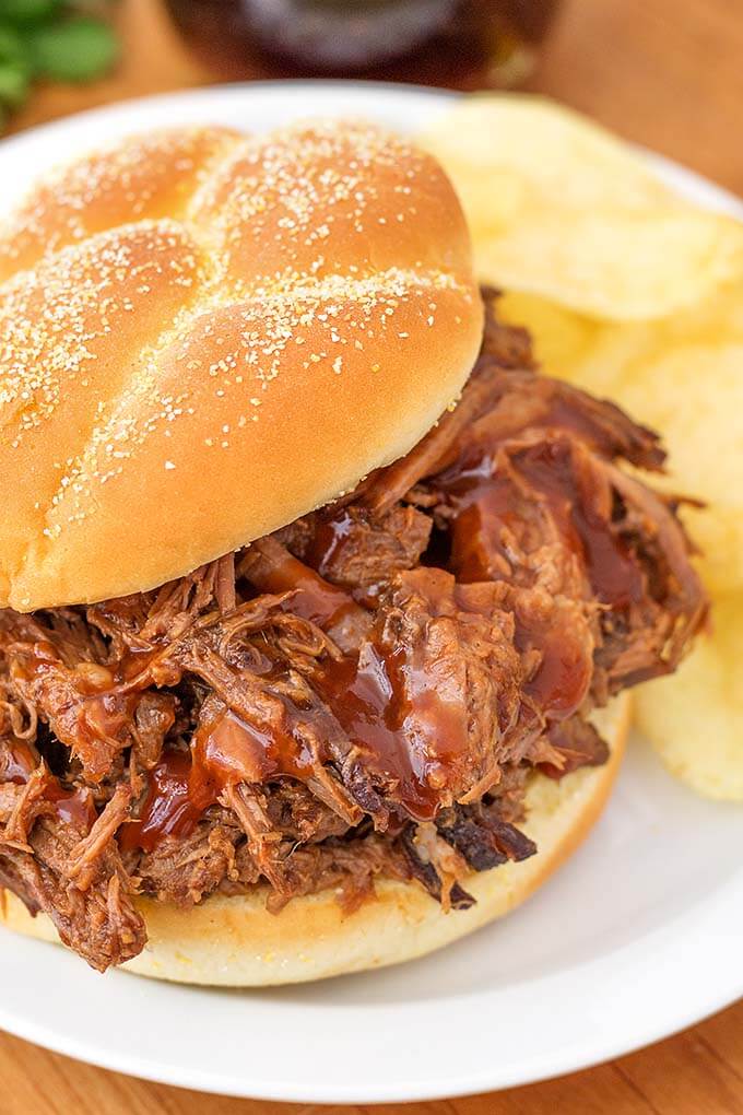 Barbecue Beef on a hamburger bun and potato chips on a white plate