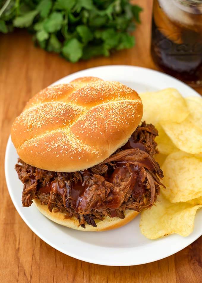 Instant Pot Barbecue Beef on a hamburger bun with potato chips on a white plate