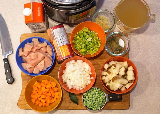 Cutting board with eight bowls containing different ingredients for chicken and dumplings along with other ingredients