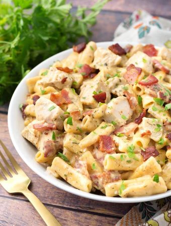 Chicken Bacon Ranch Pasta in a white bowl on wooden background with golden spoon