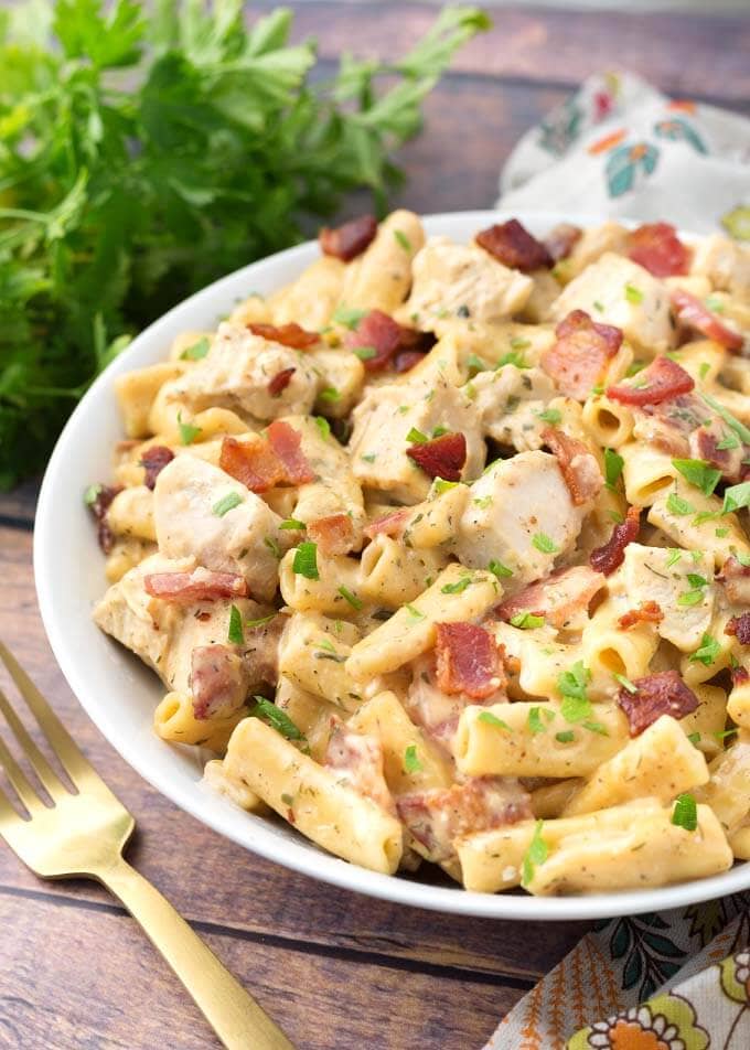 Chicken Bacon Ranch Pasta in a white bowl on wooden background with golden spoon