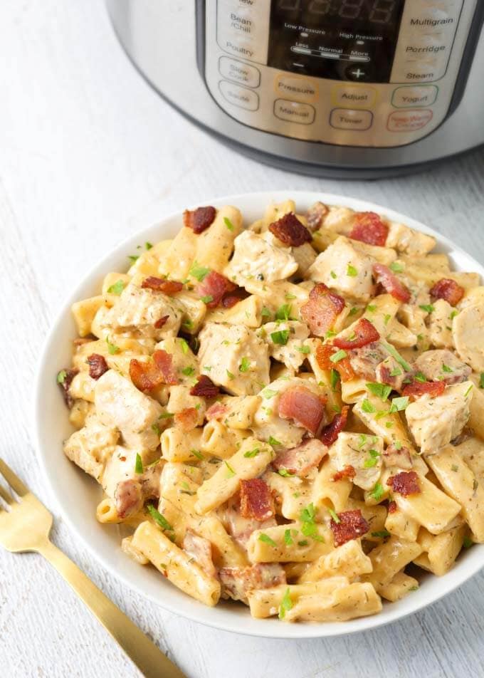 Chicken Bacon Ranch Pasta in a white bowl on light  wooden background with golden spoon with pressure cooker in background    