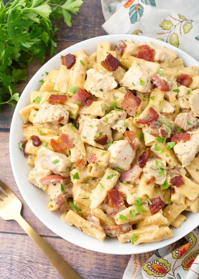 Chicken Bacon Ranch Pasta in a white bowl on wooden background with golden spoon