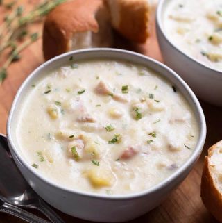 Two white bowls of Clam Chowder on a wooden board with bread rolls