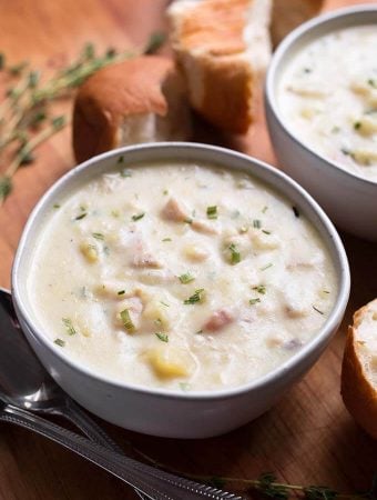 Two white bowls of Clam Chowder on a wooden board with bread rolls