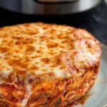 Whole round Lasagna on a light blue plate with pressure cooker in background