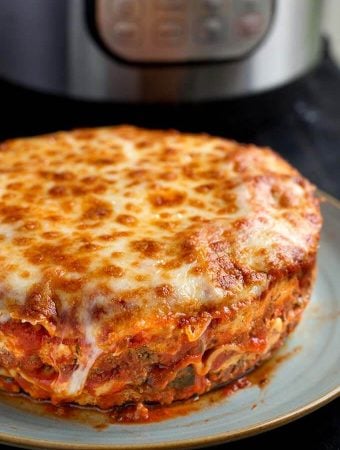 Whole round Lasagna on a light blue plate with pressure cooker in background