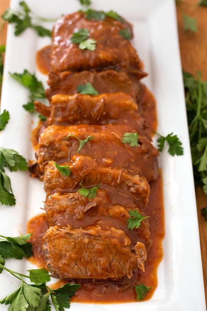 Sliced Saucy Beef Brisket on white rectangular platter garnished with green herb