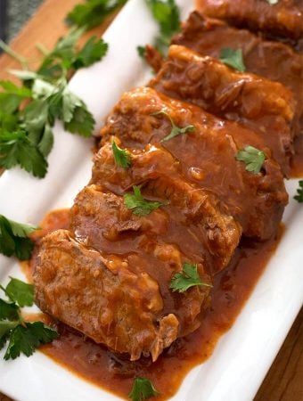 Sliced Saucy Beef Brisket on white rectangular platter garnished with green herb