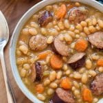 Sausage and White beans om a gray bowl next to silver spoon on wooden board