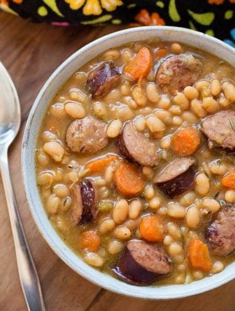 Sausage and White beans om a gray bowl next to silver spoon on wooden board