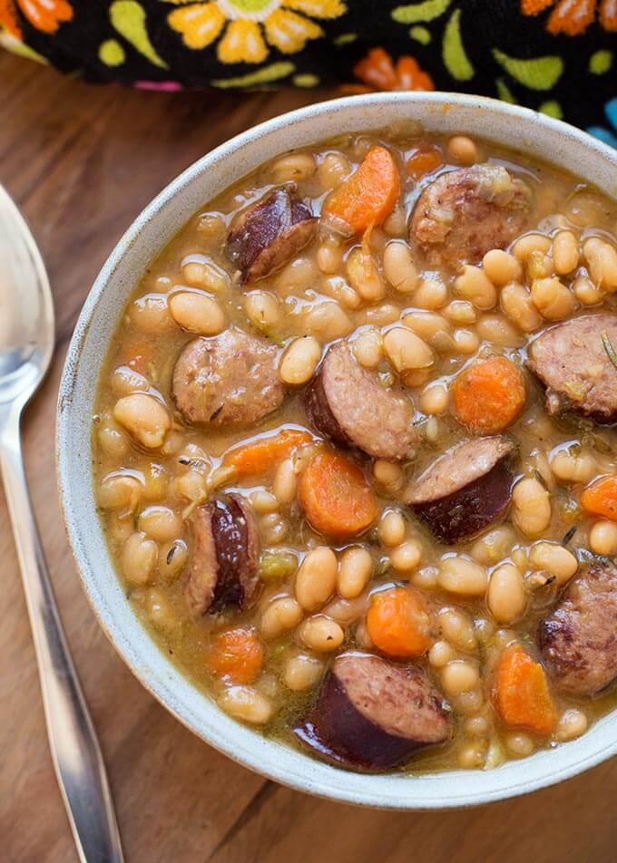 Sausage and White beans om a gray bowl next to silver spoon on wooden board