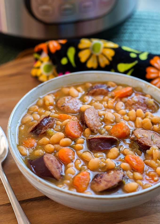 Sausage and White beans om a gray bowl next to silver spoon on wooden board