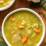 Split Pea Soup in a white bowl on wooden background with broken bread roll